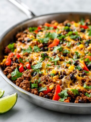 Homemade ground turkey taco skillet recipe topped with melted cheese, bell peppers, beans, corn, and fresh cilantro on a white kitchen counter.