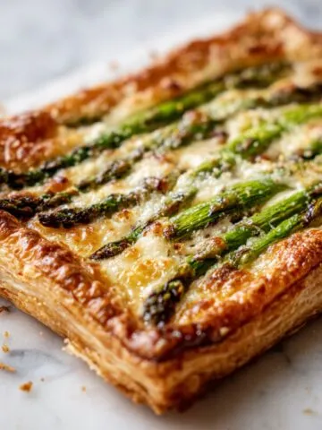 Homemade asparagus puff pastry recipe tart with melted cheese on a white marble counter, photographed from above in natural light.