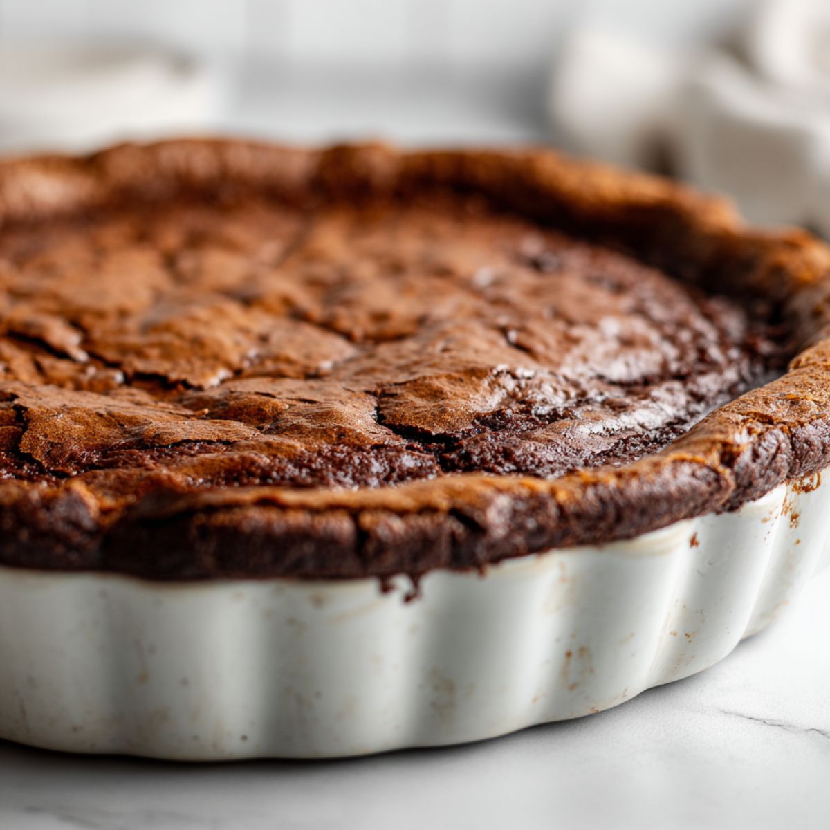 Overhead photo of a homemade brownie pie recipe in a pie dish with rustic edges on a white kitchen counter.