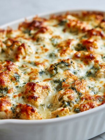 Overhead shot of a freshly baked spinach artichoke chicken casserole recipe with golden melted cheese on a white kitchen counter