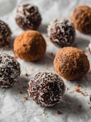 Homemade chocolate bites recipe on a white kitchen counter, some topped with coconut and nuts, photographed from above in natural light for a cozy homemade look.