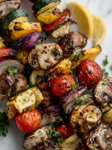 Homemade grilled veggie kabobs reciipe on a white marble counter with lemon wedges and parsley, captured from above in natural daylight.