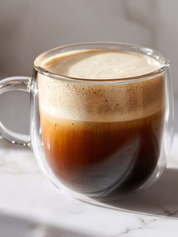 Homemade Irish Cream Coffee recipe in a glass mug with cream floating on top, shot from above on a white marble counter with natural morning light.