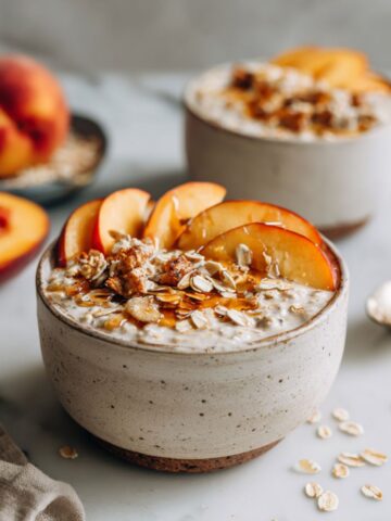 Homemade peach cobbler overnight oats recipe jar topped with fresh peaches and granola on a white marble counter, photographed from above in natural morning light.