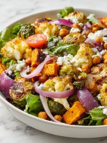 Overhead shot of a homemade roasted salad recipe with sweet potatoes, cauliflower, Brussels sprouts, and feta on a white kitchen counter.