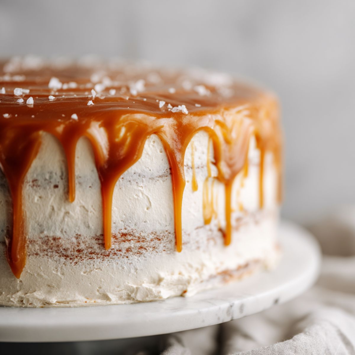 Overhead view of a homemade salted caramel cake recipe with caramel drips and sea salt flakes on a white kitchen counter.
