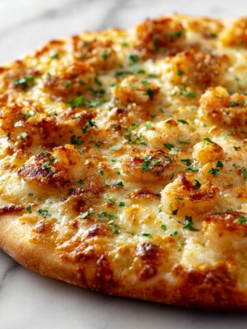 Homemade shrimp scampi pizza recipe with golden crust, garlic butter sauce, and melted cheese on a white kitchen counter, photographed from above.