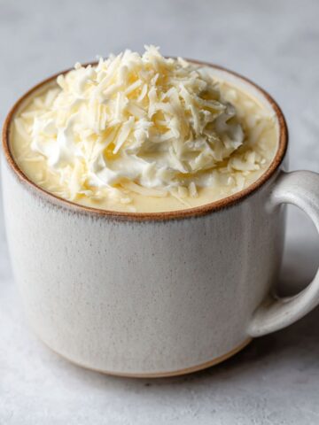 “Homemade white chocolate hot chocolate recipe topped with whipped cream and chocolate shavings on a white marble counter, cozy winter setting, overhead shot”