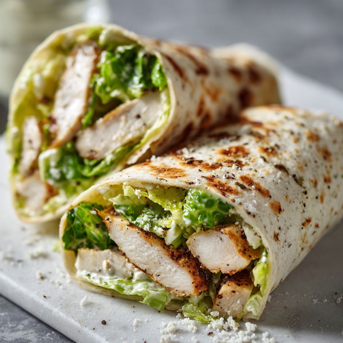 Overhead shot of a homemade chicken Caesar salad wrap recipe sliced in half on a white kitchen counter with natural light, looking casual and freshly made.