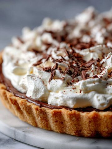Homemade French Silk Chocolate Pie Recipe topped with whipped cream and chocolate shavings on a white kitchen counter.
