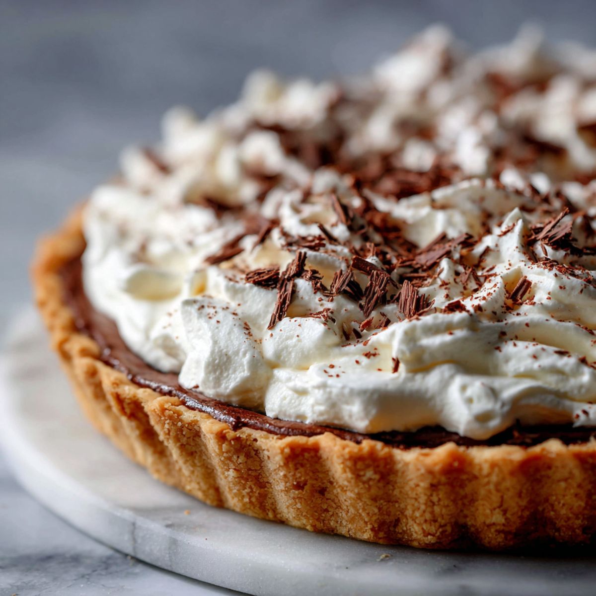 Homemade French Silk Chocolate Pie Recipe topped with whipped cream and chocolate shavings on a white kitchen counter.