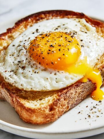 Overhead view of homemade fried egg toast recipe with runny yolk on white marble counter, served simply with black pepper.