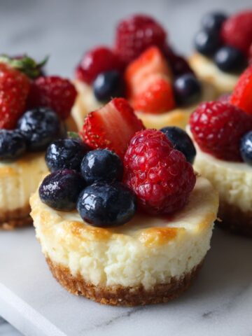 Homemade fruit cheesecake bites recipe topped with fresh berries on a white marble kitchen counter, captured from an overhead angle in natural light.