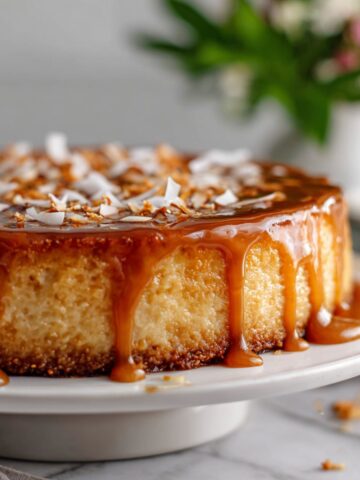 Homemade coconut flan cake recipe with golden caramel dripping down the sides on a white kitchen counter, photographed from above with a natural, homemade feel