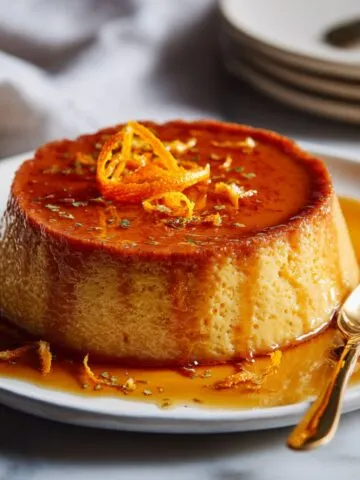 Flat lay of ingredients for homemade orange flan recipe including fresh oranges, eggs, condensed milk, evaporated milk, and sugar on a white kitchen counter in natural light with a slightly messy, homemade look.
