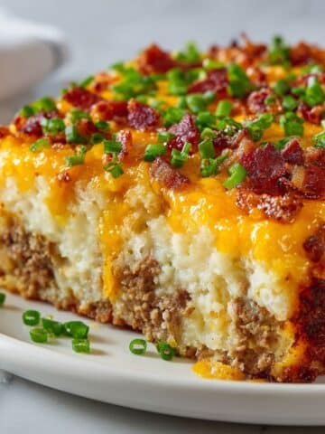 “Homemade loaded mashed potato meatloaf casserole recipe topped with melted cheese, crispy bacon, and green onions on a white marble counter.”
