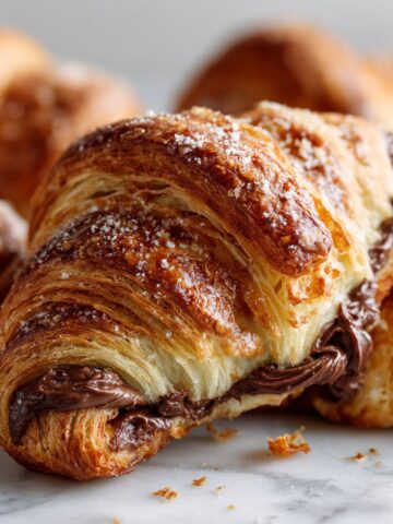 Overhead shot of golden homemade Nutella croissants recipe on a white kitchen counter, looking warm, flaky, and freshly baked with a cozy homemade feel.