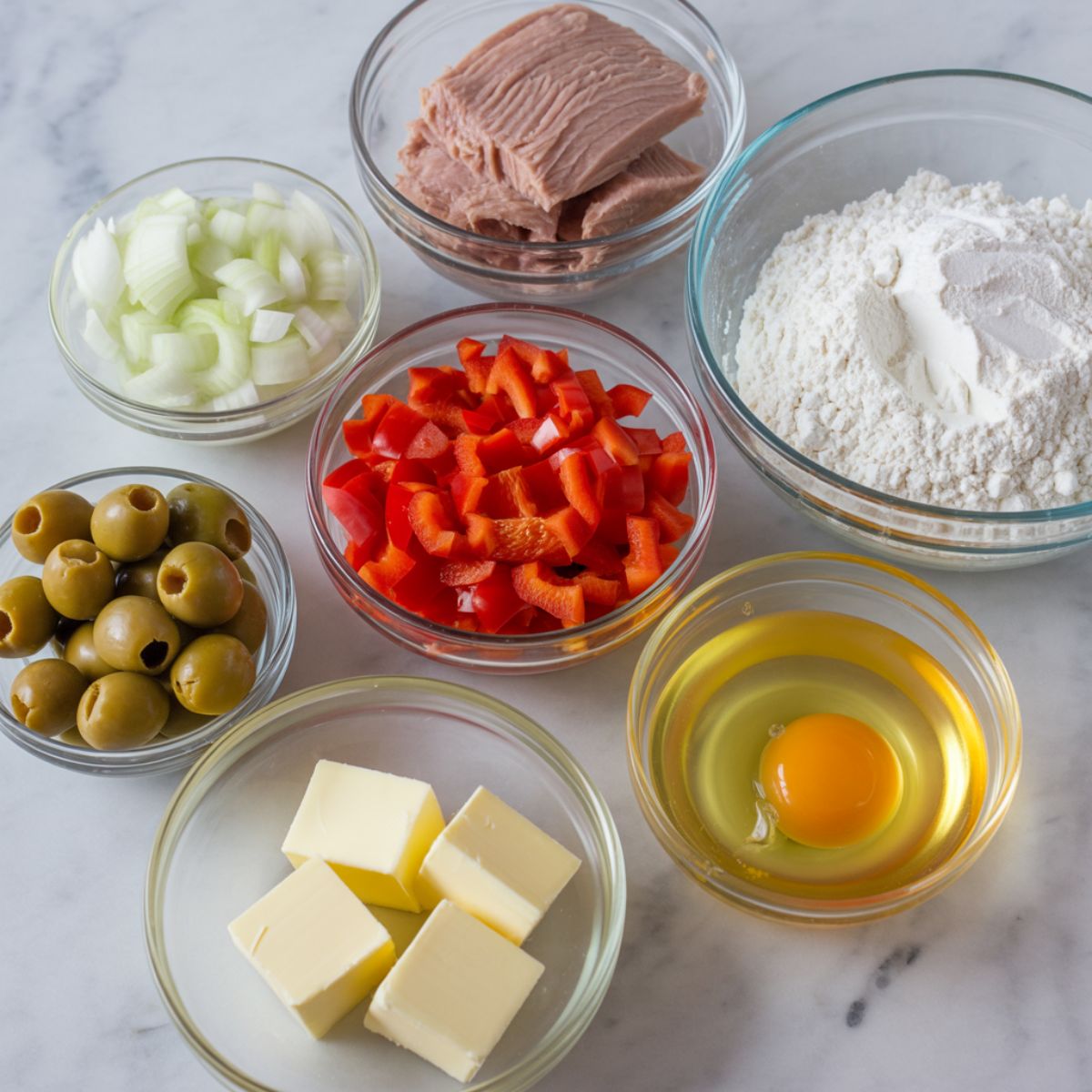 Real homemade tuna empanadas ingredients arranged casually on a white kitchen counter, including tuna, eggs, bell pepper, flour, and butter, photographed from above in natural light.