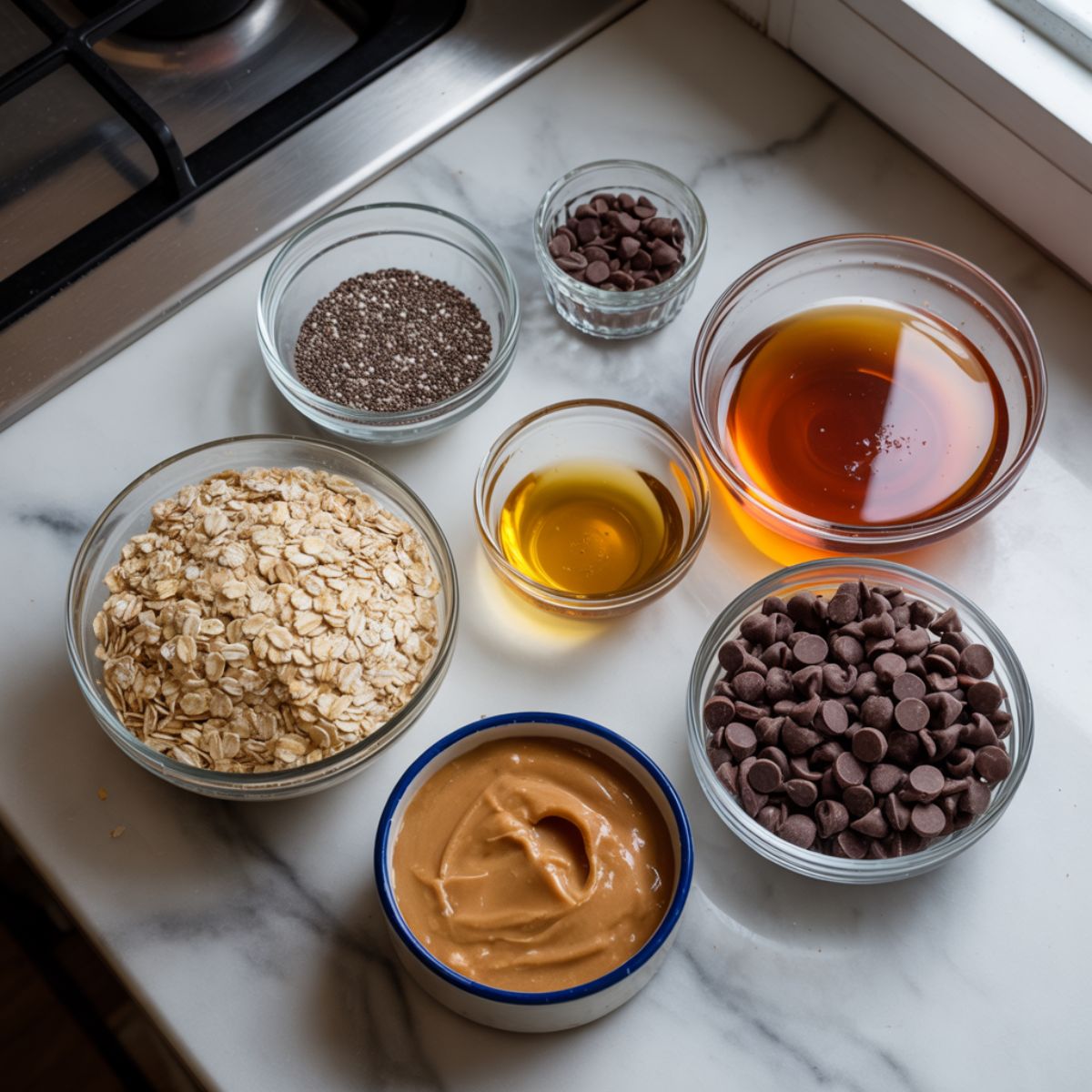 “Chia seed energy bites ingredients — oats, chia seeds, peanut butter, honey, and chocolate chips — arranged casually on a white marble kitchen counter.”