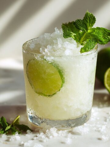 Overhead photo of a homemade coconut mocktail recipe on a white marble kitchen counter with lime and mint garnish, looking refreshing and natural.
