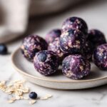 Overhead photo of homemade blueberry energy balls recipe on a white marble counter with scattered oats and dried blueberries.