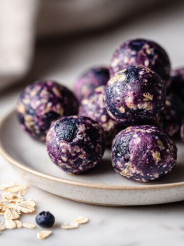 Overhead photo of homemade blueberry energy balls recipe on a white marble counter with scattered oats and dried blueberries.