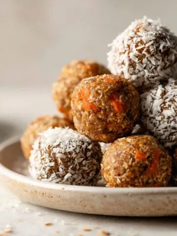 Homemade carrot cake energy balls recipe on a white marble counter with coconut coating and fresh carrot bits, photographed from above in natural light.