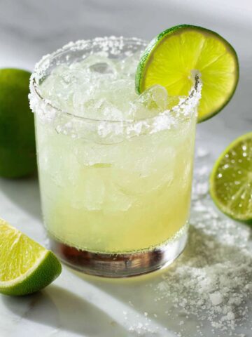 “Homemade margarita mocktail recipe with salt rim and lime wedge on a white kitchen counter, photographed from above.”