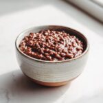 Homemade chocolate rice pudding recipe in a ceramic bowl on a white kitchen counter, photographed from above in natural light, showing its rich creamy texture and cozy homemade feel.