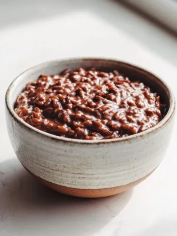Homemade chocolate rice pudding recipe in a ceramic bowl on a white kitchen counter, photographed from above in natural light, showing its rich creamy texture and cozy homemade feel.