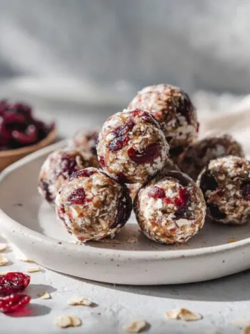 Overhead photo of homemade cranberry energy balls recipe on a white marble counter with scattered oats and cranberries, looking rustic and real.