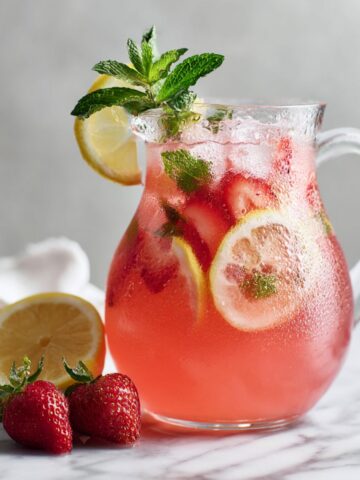 Overhead shot of homemade strawberry lemonade with mint recipe and lemon slices on a white marble counter, photographed naturally with a real, homemade feel.