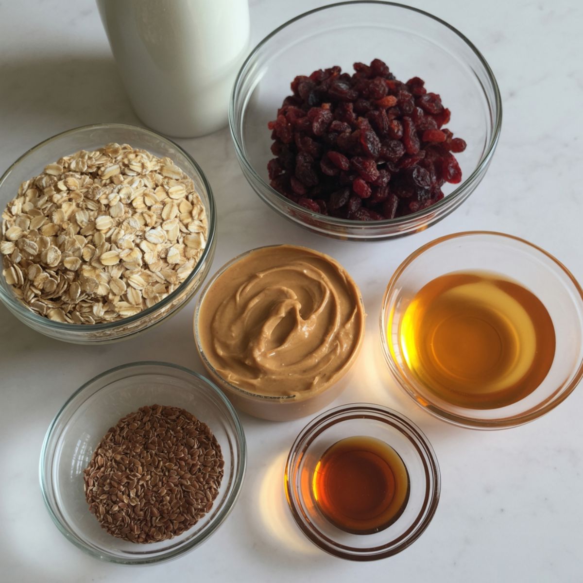 Overhead shot of messy but real ingredients for cranberry energy balls including oats, cranberries, peanut butter, and honey on a white kitchen counter.
