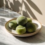 Overhead view of homemade matcha green tea mochi recipe balls on a white marble counter, dusted with cornstarch and slightly uneven for a natural, handmade look.