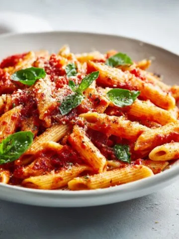 Homemade penne marinara pasta recipe served on a white kitchen counter with basil and parmesan, photographed from overhead in natural light.