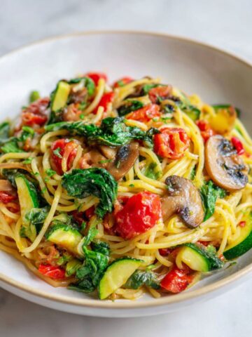 “Homemade veggie spaghetti recipe with colorful vegetables and tomato sauce on a white marble counter, photographed from above in natural light.”